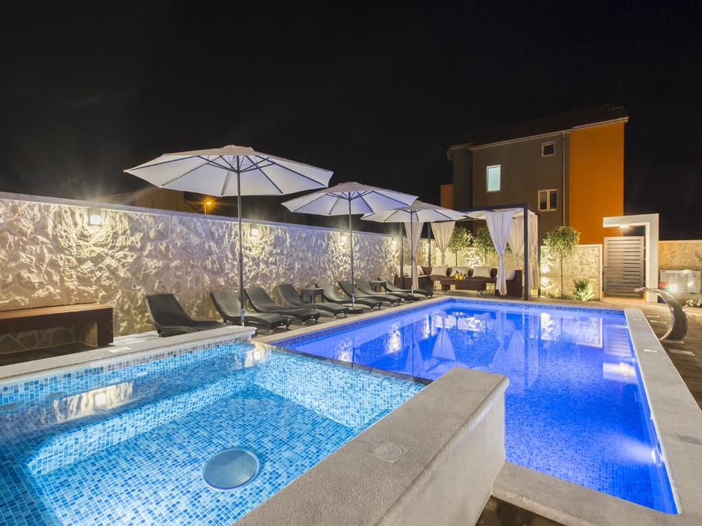 a swimming pool with chairs and umbrellas at night at Grebastica Poolside Villa in Grebaštica