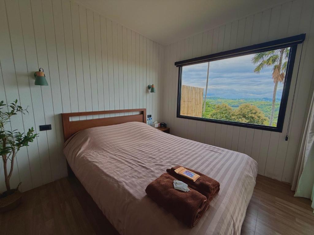 a bedroom with a bed with a large window at หรรษาวิว ที่พักเขาค้อ เพชรบูรณ์ in Khao Kho
