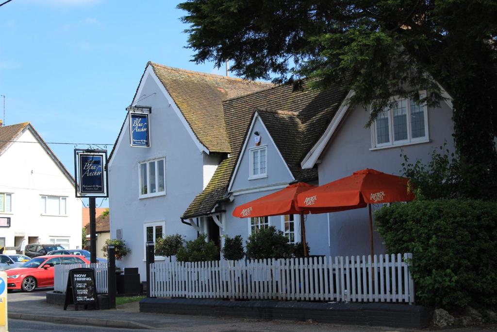 a white building with a white fence and red umbrellas at The Blue Anchor in Feering