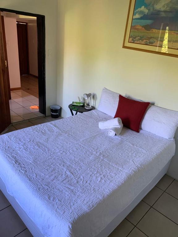 a large white bed with a red pillow on it at Ezulwini Thatch in Ezulwini