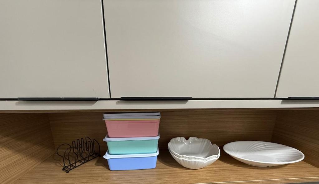 a kitchen with a shelf with bowls and a microwave at Apartamento pé na areia em Tramandaí in Tramandaí