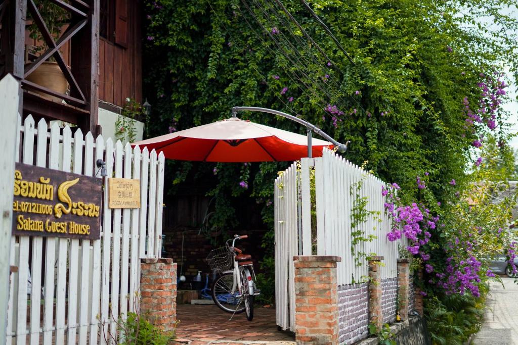 a white fence with a red umbrella next to a building at Sarana Guest House in Luang Prabang