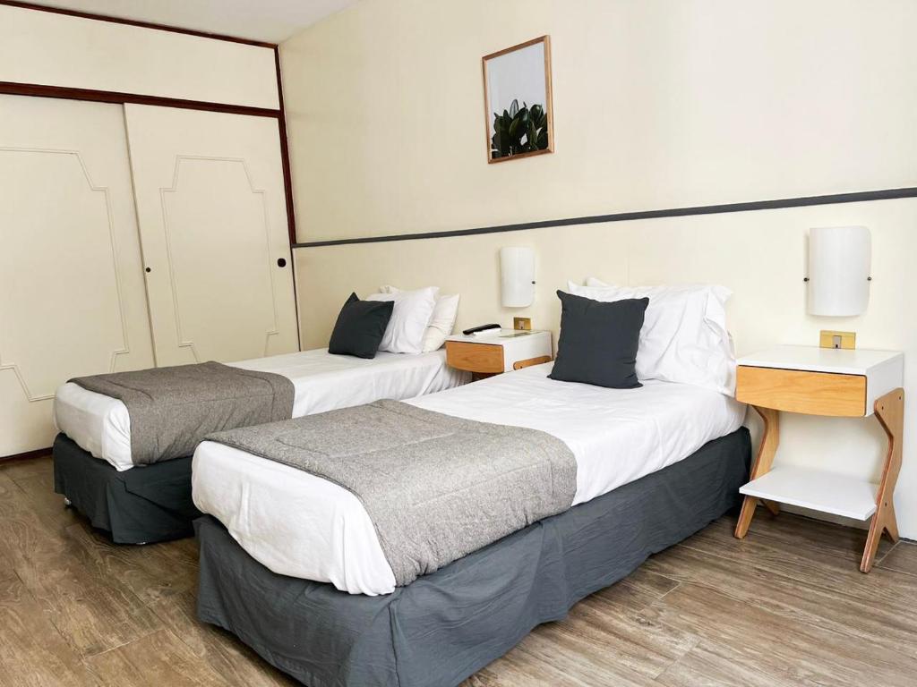 two beds in a hotel room with two tables at Alpino Hotel in Buenos Aires