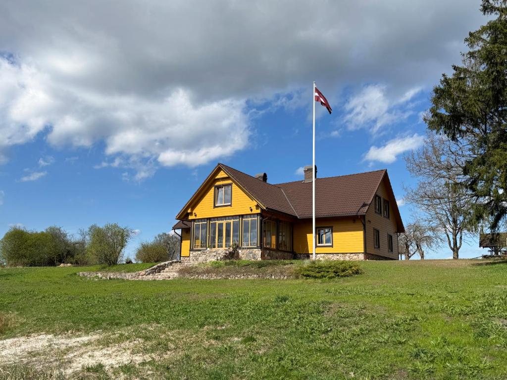 a yellow house with a flag on top of it at Mazmuiža in Lenči