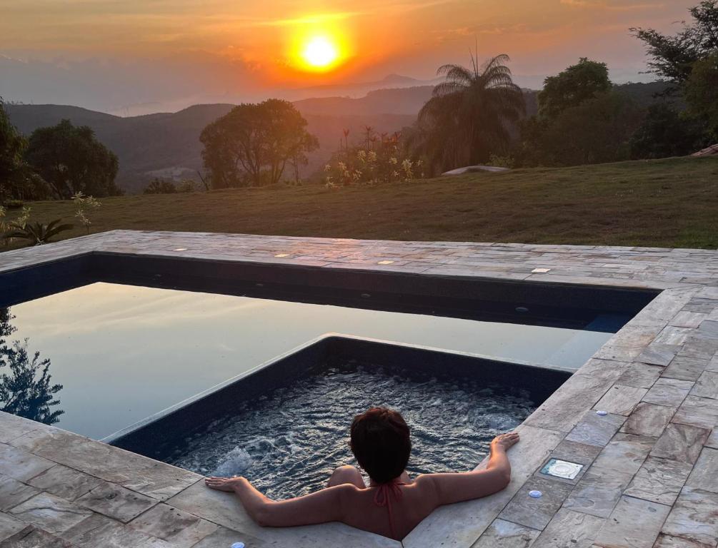 Una mujer sentada en una piscina mirando la puesta de sol en Recanto da Natureza, en Itabirito