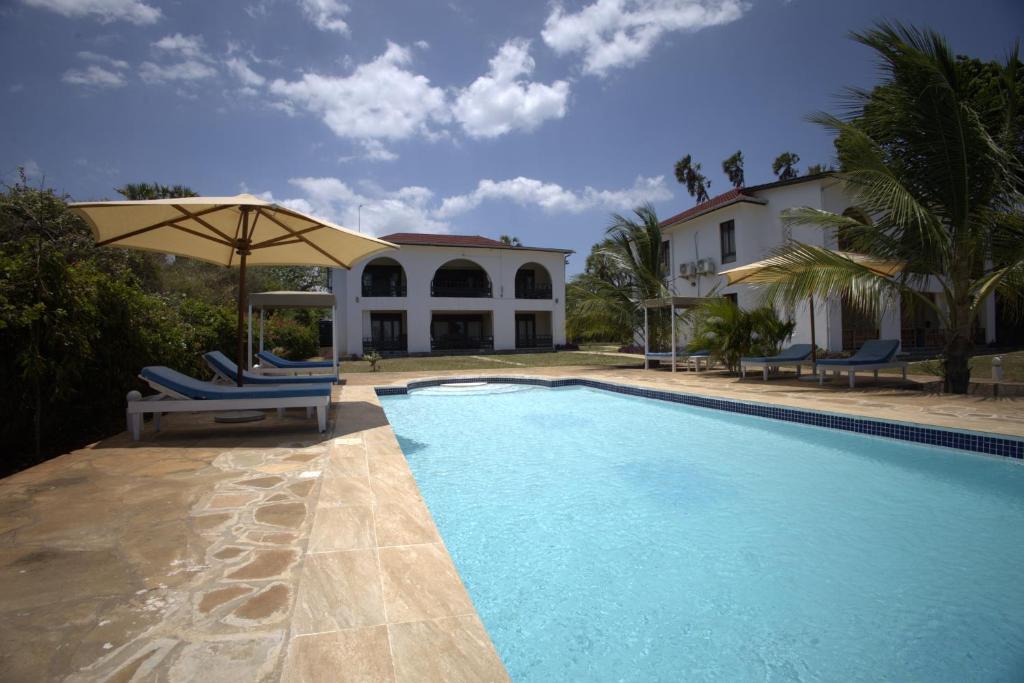 a swimming pool with chairs and an umbrella next to a house at Munje Luxury Beach Villas in Msambweni
