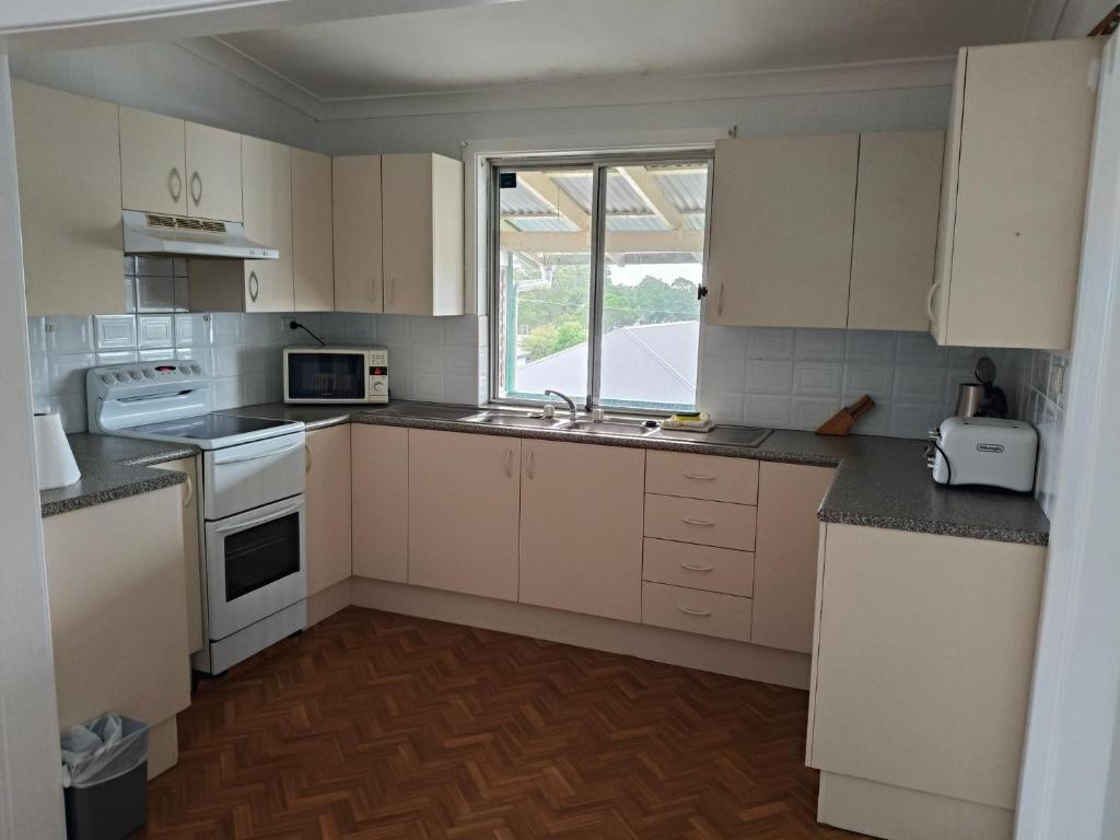 eine Küche mit weißen Schränken und einer Spüle und einem Fenster in der Unterkunft Coconut Cottage - Sanctuary Point in Sanctuary Point