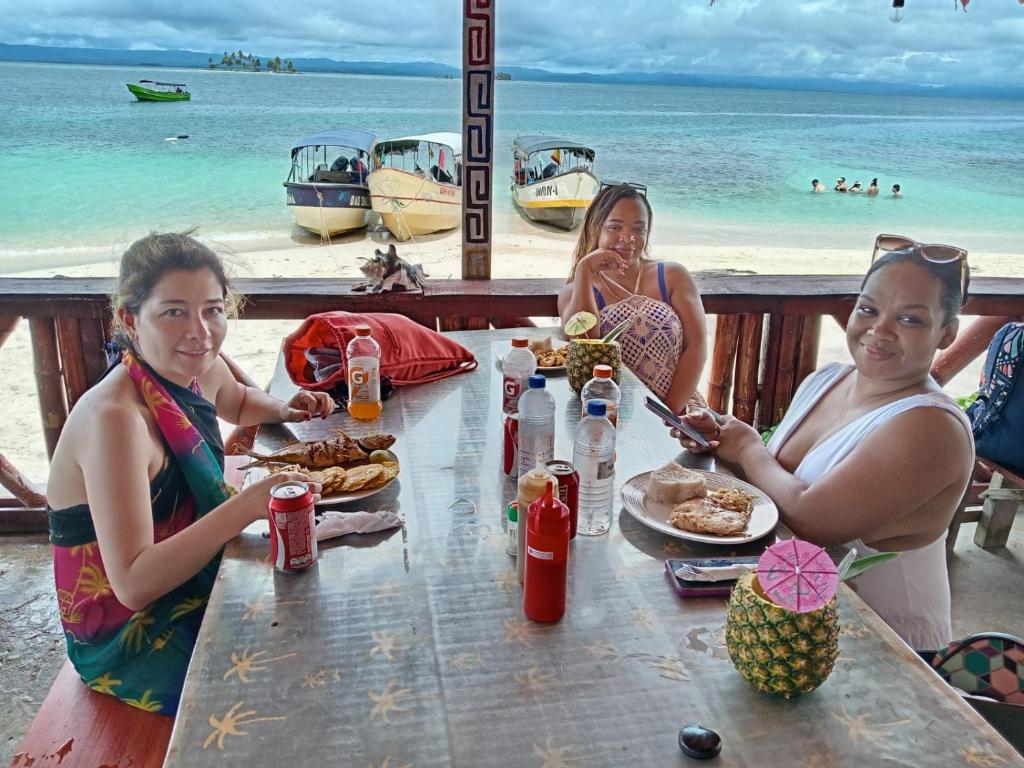 Cayos Los Grullosにあるamazing gunayarのビーチでテーブルに座り、食事をする3人の女性