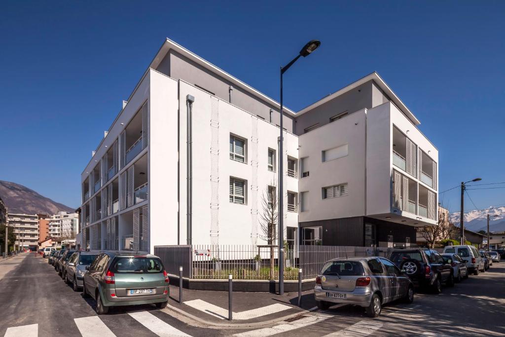 un bâtiment blanc avec des voitures garées dans un parking dans l'établissement Tempologis Grenoble, à Grenoble
