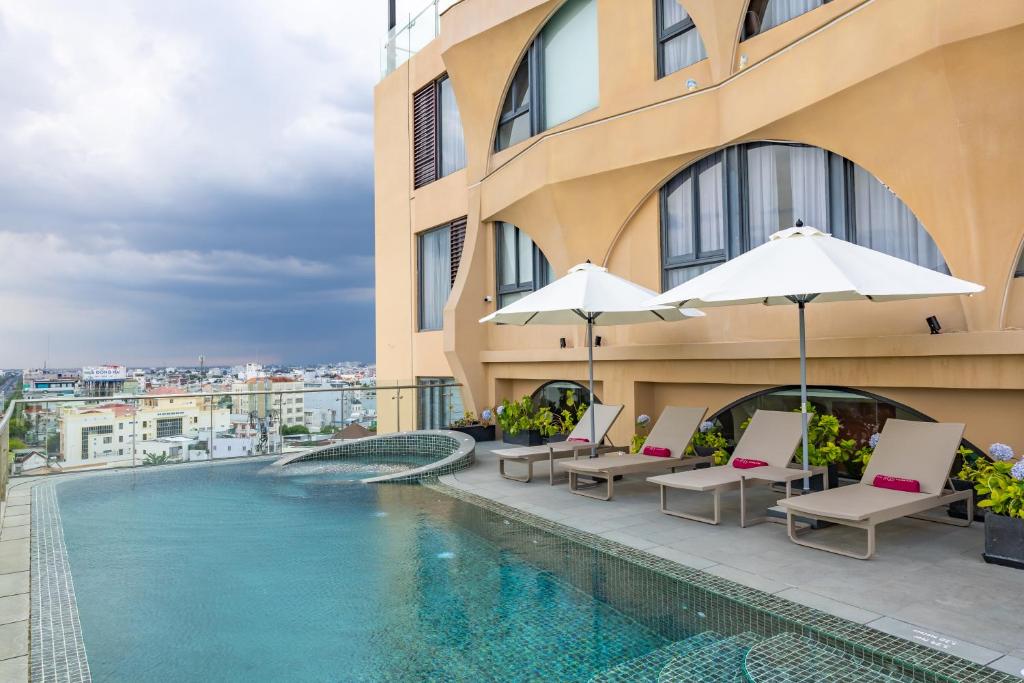 a swimming pool with chairs and umbrellas next to a building at The IRIS SIGNATURE HOTEL AND SPA in Can Tho