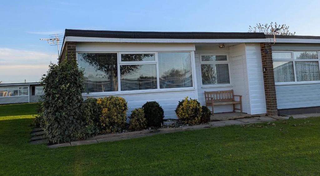 a white house with a bench in the front yard at 145, Two bed newly refurbished chalet on Sund0wner Holiday Park - Sleeps 5, pet friendly - Includes bed linen and towels plus electricity in Great Yarmouth