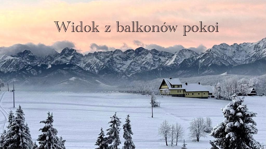 a snow covered field with a house and mountains at Muzyczny Dworek in Rzepiska