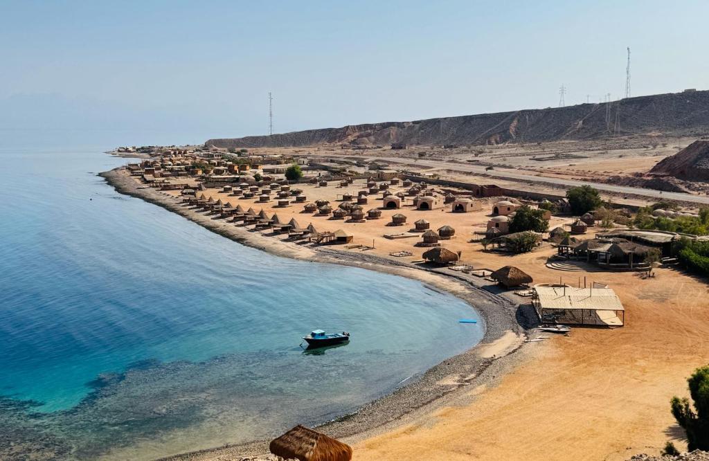 einen Strand mit Sonnenschirmen und einem Boot im Wasser in der Unterkunft Luna Camp in Nuweiba