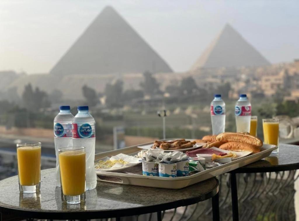 uma mesa com uma bandeja de comida e garrafas de sumo de laranja em AKEN Pyramids View em Cairo