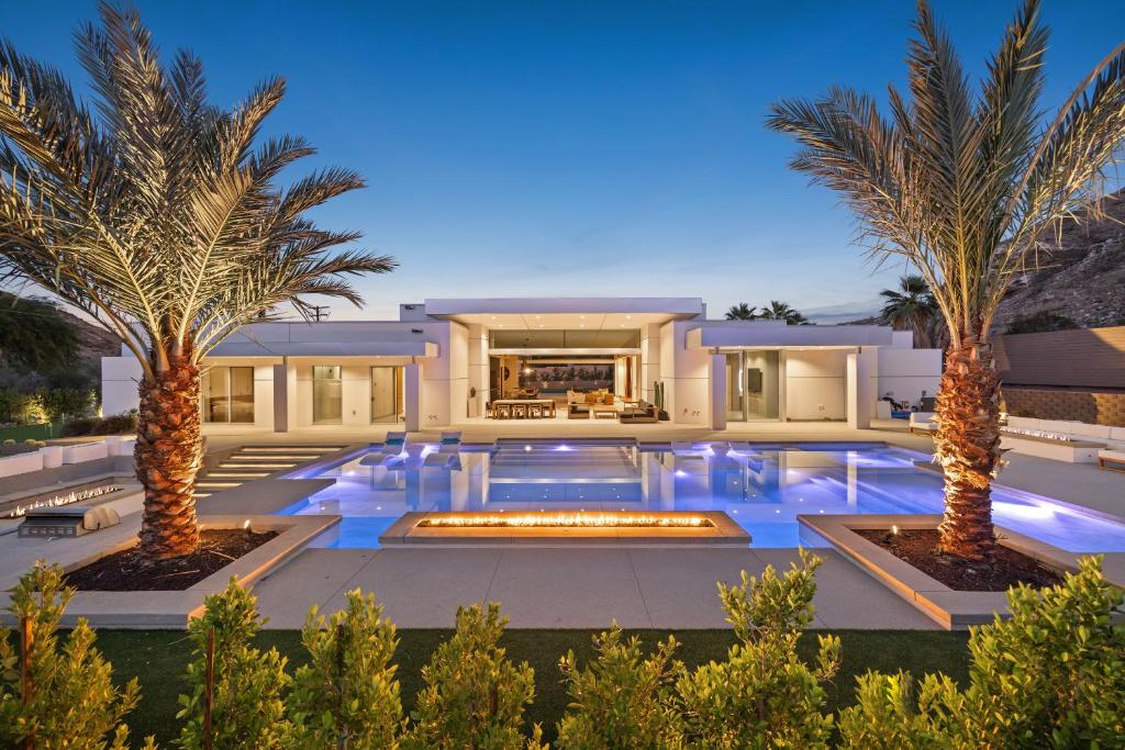 a villa with a swimming pool and two palm trees at The Desert Wellness Compound in Palm Desert
