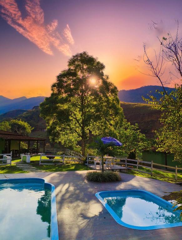two pools in a yard with a sunset in the background at Rancho Pôr Do Sol in Arapeí