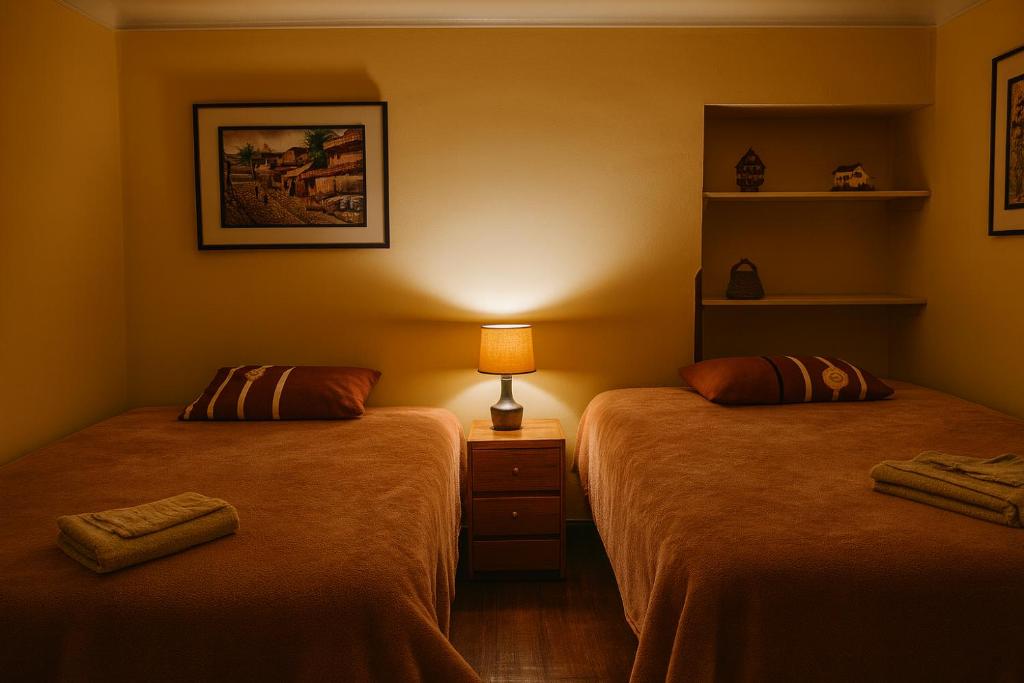 two beds in a room with a lamp on a table at Panay Golden in Cusco
