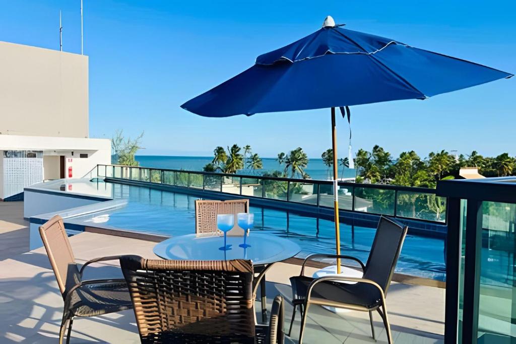 eine Terrasse mit Tisch und Stühlen und einem Sonnenschirm in der Unterkunft Flat Praia de Maracaípe - Porto de Galinhas in Porto De Galinhas