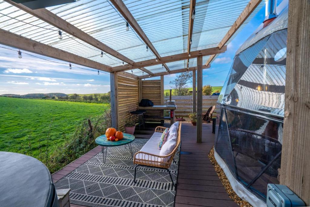 a patio with a roof with a table and chairs at Coorie Retreats Luxury Geo Domes and Cabins with Private Hot Tubs Cinema Firepit Spa and More in Portpatrick