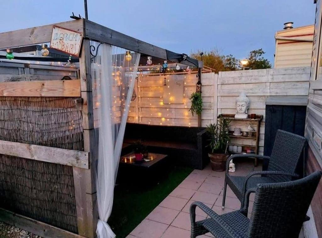 eine Terrasse mit 2 Stühlen und einem Zaun mit Licht in der Unterkunft Tiny Beach Cottage - New Vennepark Wenduine in De Haan