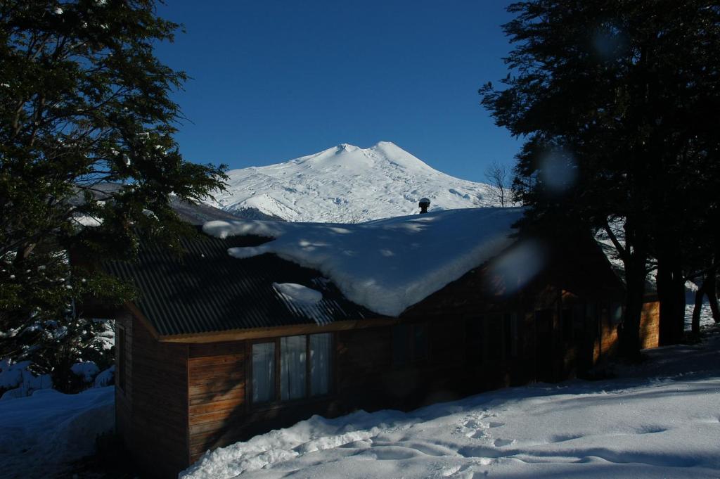 a snow covered roof of a house with a snow covered mountain at Vista Hermosa Conguillio in Conguillío