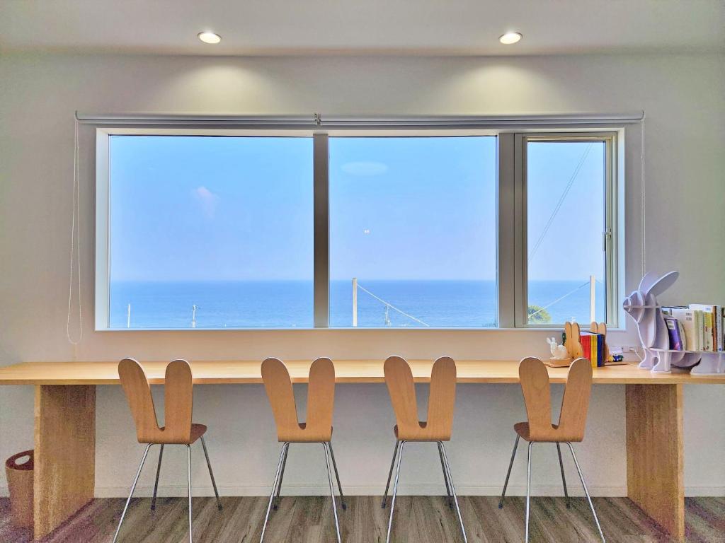 a table with four chairs in front of a large window at 「淡路島一棟貸宿　野うさぎ 」高台から海を望む貸別荘！2023年新築離れの素泊まり in Noda