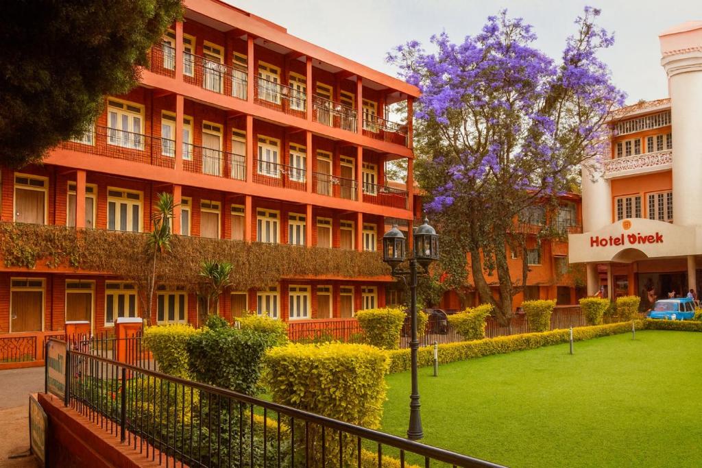 a red building with a green lawn in front of it at Hotel Vivek in Coonoor