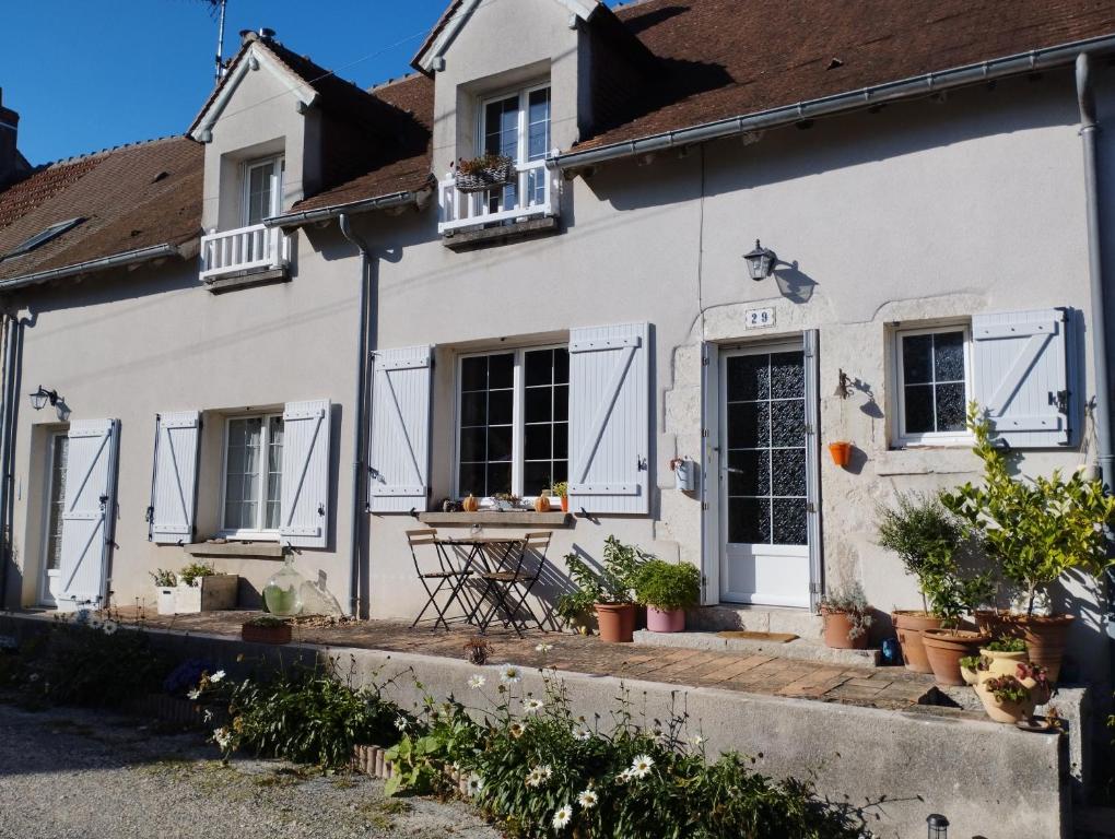 a white house with white shutters and potted plants at À fleur de source in Mer