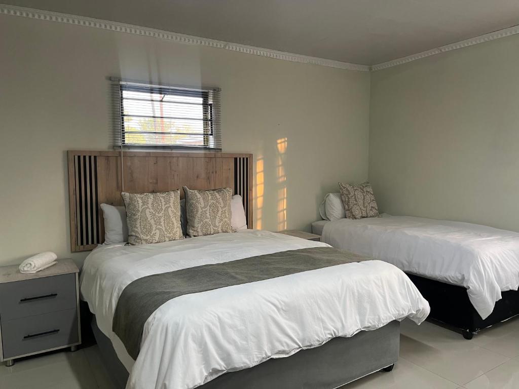 1 dormitorio con 2 camas con sábanas blancas y ventana en Sunray Guesthouse, en Newcastle