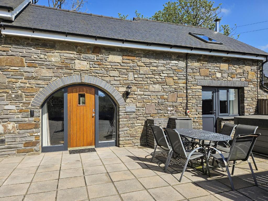 a patio with a table and chairs in front of a stone building at Cartws-Oh3 in Dihewid