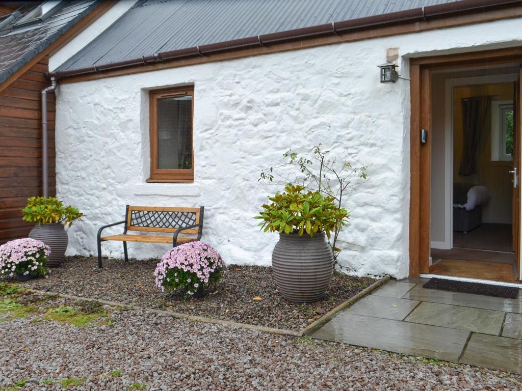 a bench in front of a white building with potted plants at Blackmill Cottages No 2 in Taynuilt