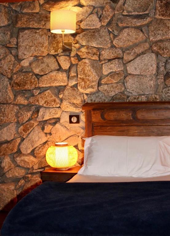 a bedroom with a stone wall with a bed and a lamp at Bergerie du Prunelli in Cauro