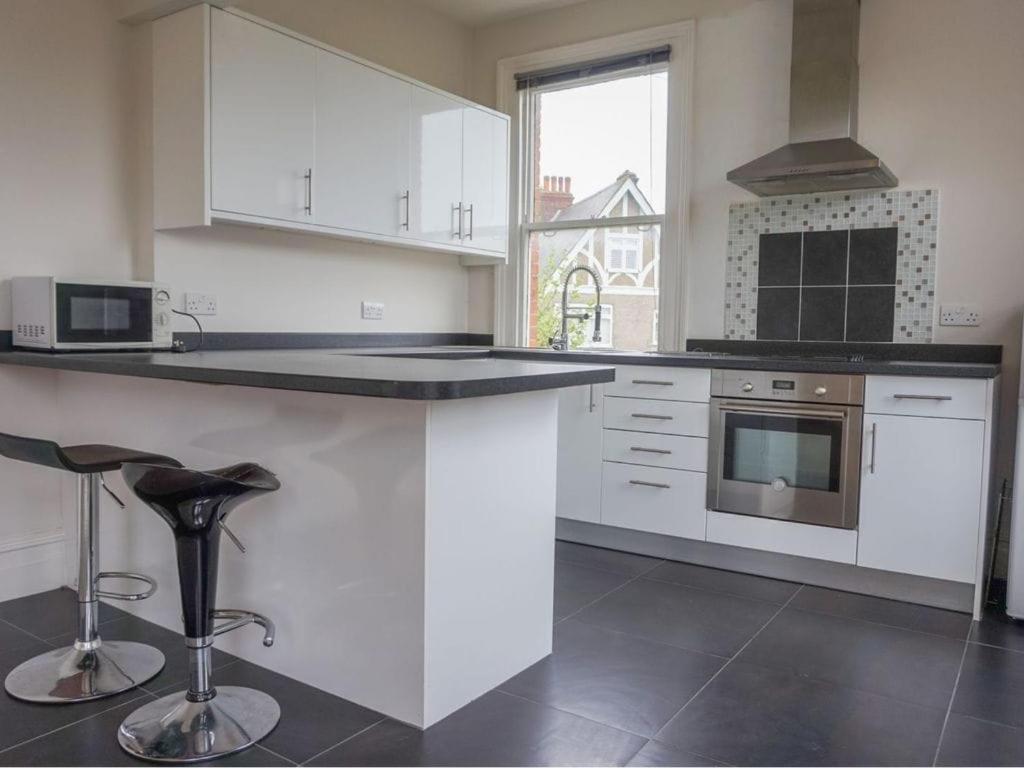 a kitchen with white cabinets and a counter with stools at Newly refurbished flat with Free Parking in Purley