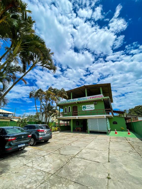 a green building with cars parked in a parking lot at Pousada Verdes Mares in Rio das Ostras