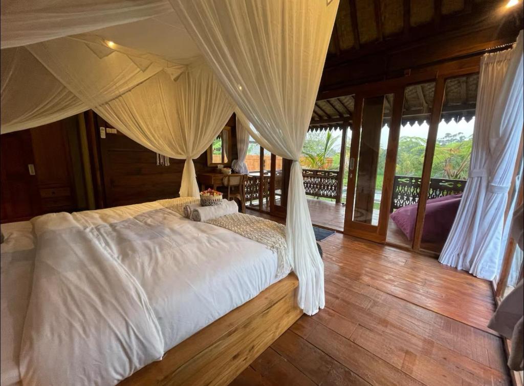 a bedroom with a bed with white sheets and curtains at Umah Jati Villa in Penginyahan