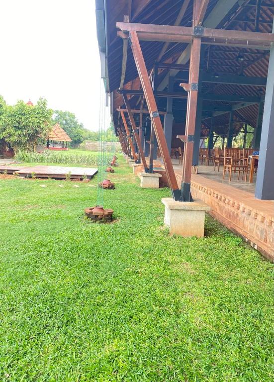a large building with a grassy yard with wooden beams at The Thinnai Farm in Jaffna