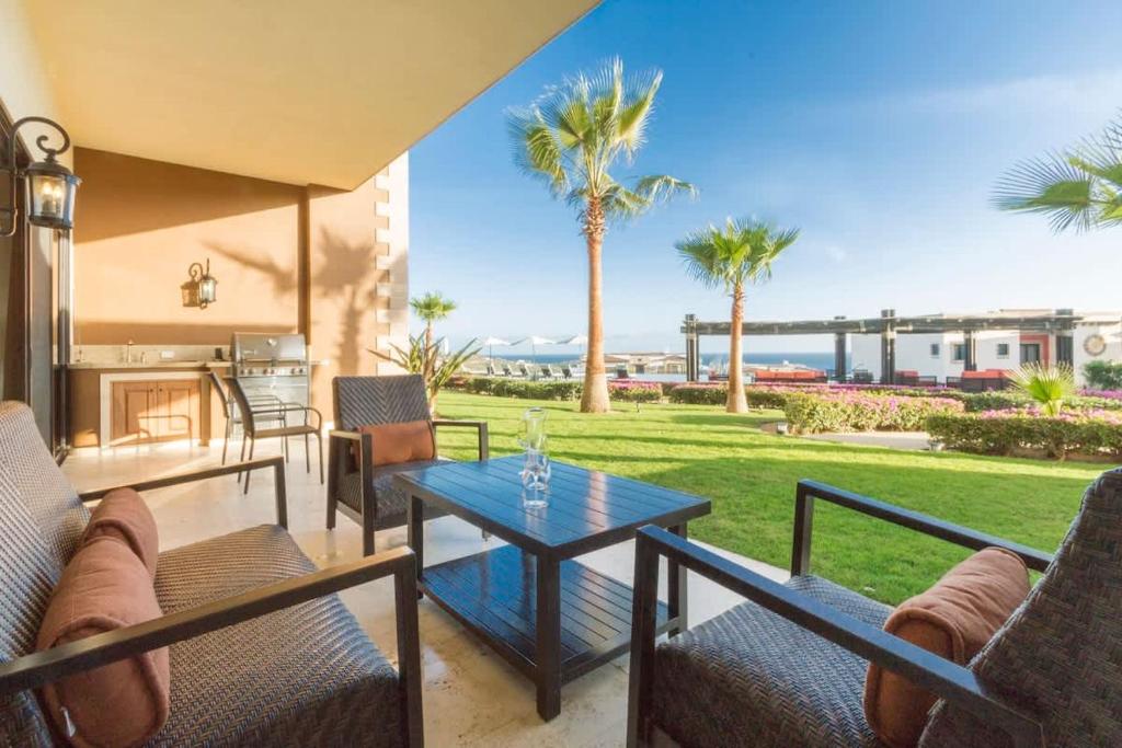 a patio with a table and chairs and palm trees at Copala At Quivira-Poolside Ground Floor Oceanview in Cabo San Lucas
