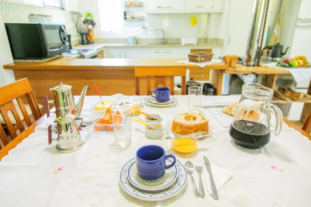 Una mesa con un mantel blanco con comida encima. en Casa do Reiki - Descanso com Café da Manhã Incluso, en Rancho Queimado