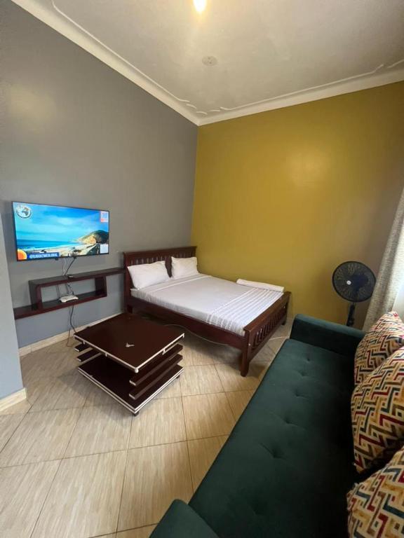 a room with a bed and a couch and a tv at Pearl suites - Bukoto in Kampala
