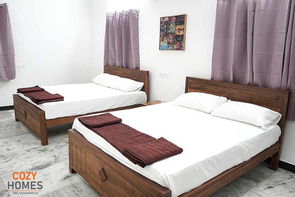 2 Betten in einem Zimmer mit lila Vorhängen in der Unterkunft Cozy Homes, Tiruvannamalai in Tiruvannāmalai