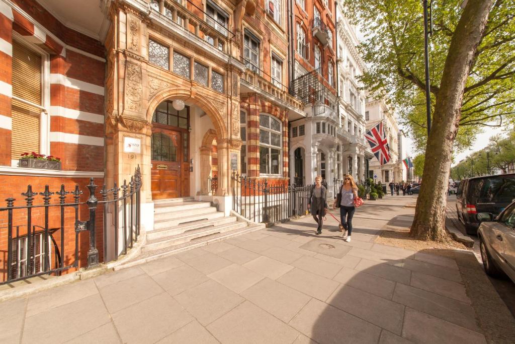 ロンドンにあるアスター ハイド パーク ホステルの二人の建物前の歩道を歩く