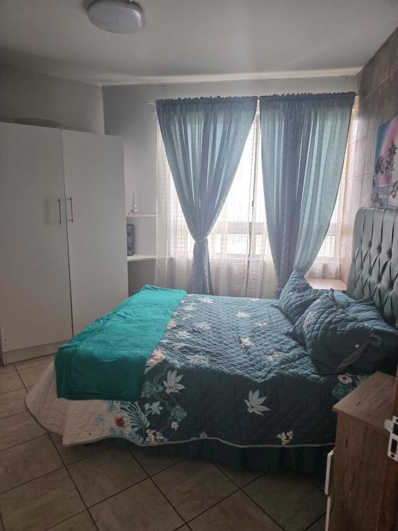 a bedroom with a bed and a window with blue curtains at Wave Watcher in Amanzimtoti