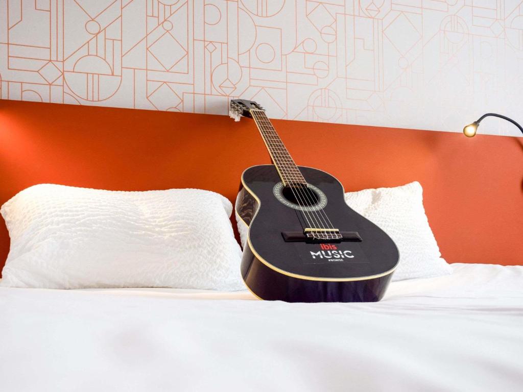 a guitar is sitting on top of a bed at ibis Rodez Centre in Rodez