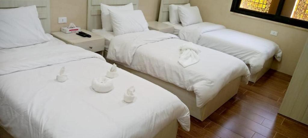 three beds in a room with white sheets and pillows at النزل الفندقي مدينة الأمير هاشم بن عبدالله الثاني للشباب in Dulaylat al Ḩamāʼidah