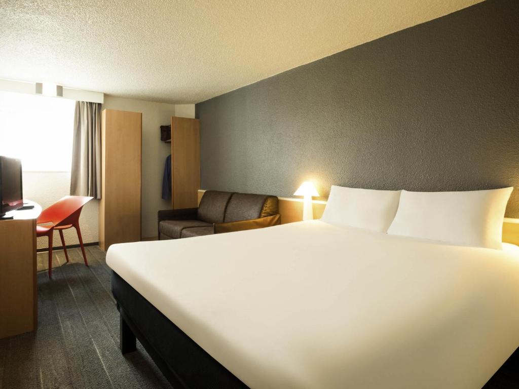 a hotel room with a large white bed and a chair at Ibis Orly Chevilly Tram 7 in Chevilly-Larue