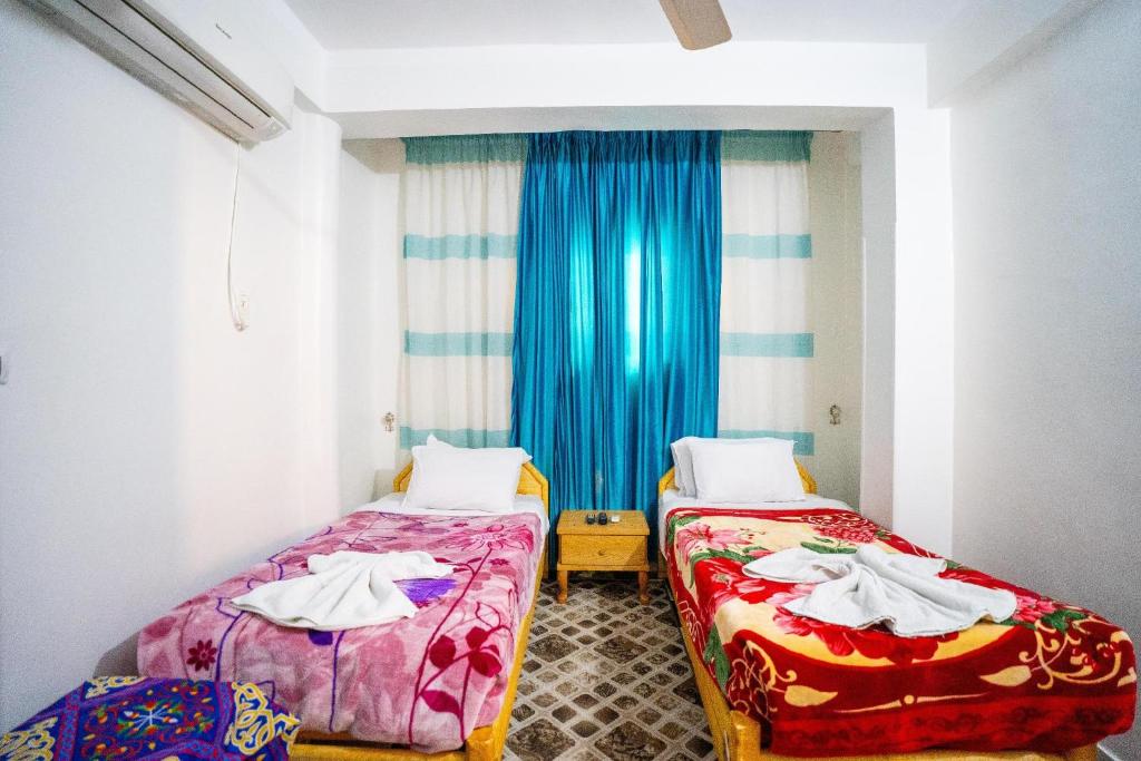 a room with two beds and a window with blue curtains at Luxor Nile Palace in Luxor
