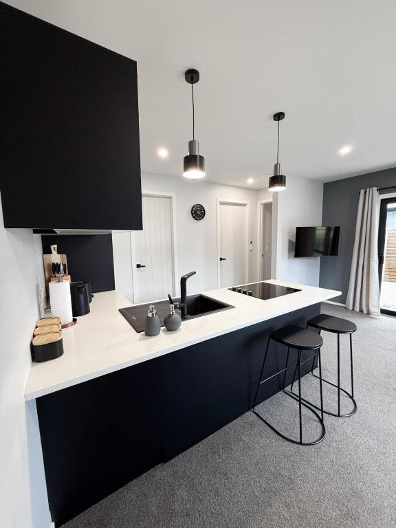 Una cocina en blanco y negro con fregadero y taburetes. en Private self contained unit, en Pukekohe East