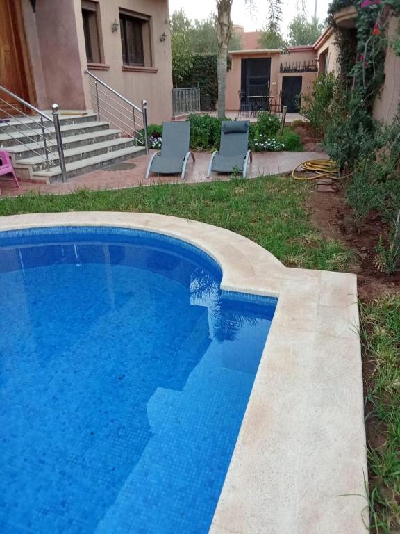 a blue swimming pool with two chairs and a house at Villa Amroth in Marrakech