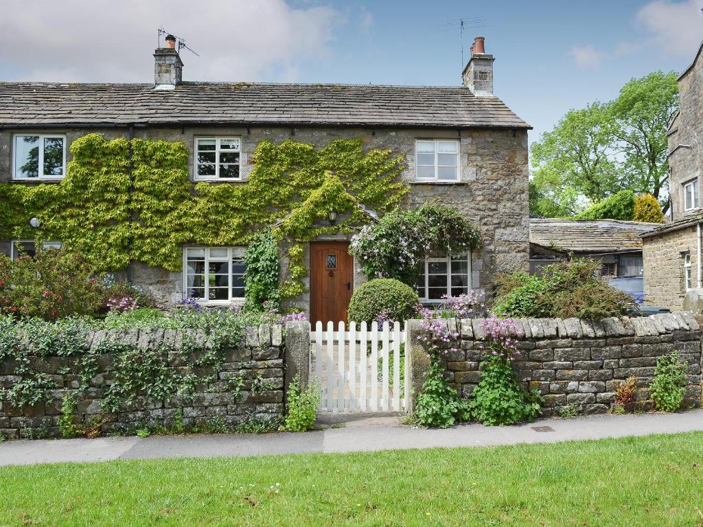 a stone house with a white picket fence at Clematis Cottage in Burnsall