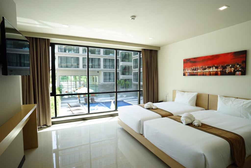 two beds in a room with a large window at Beston Pattaya - SHA Plus Certified in Pattaya South